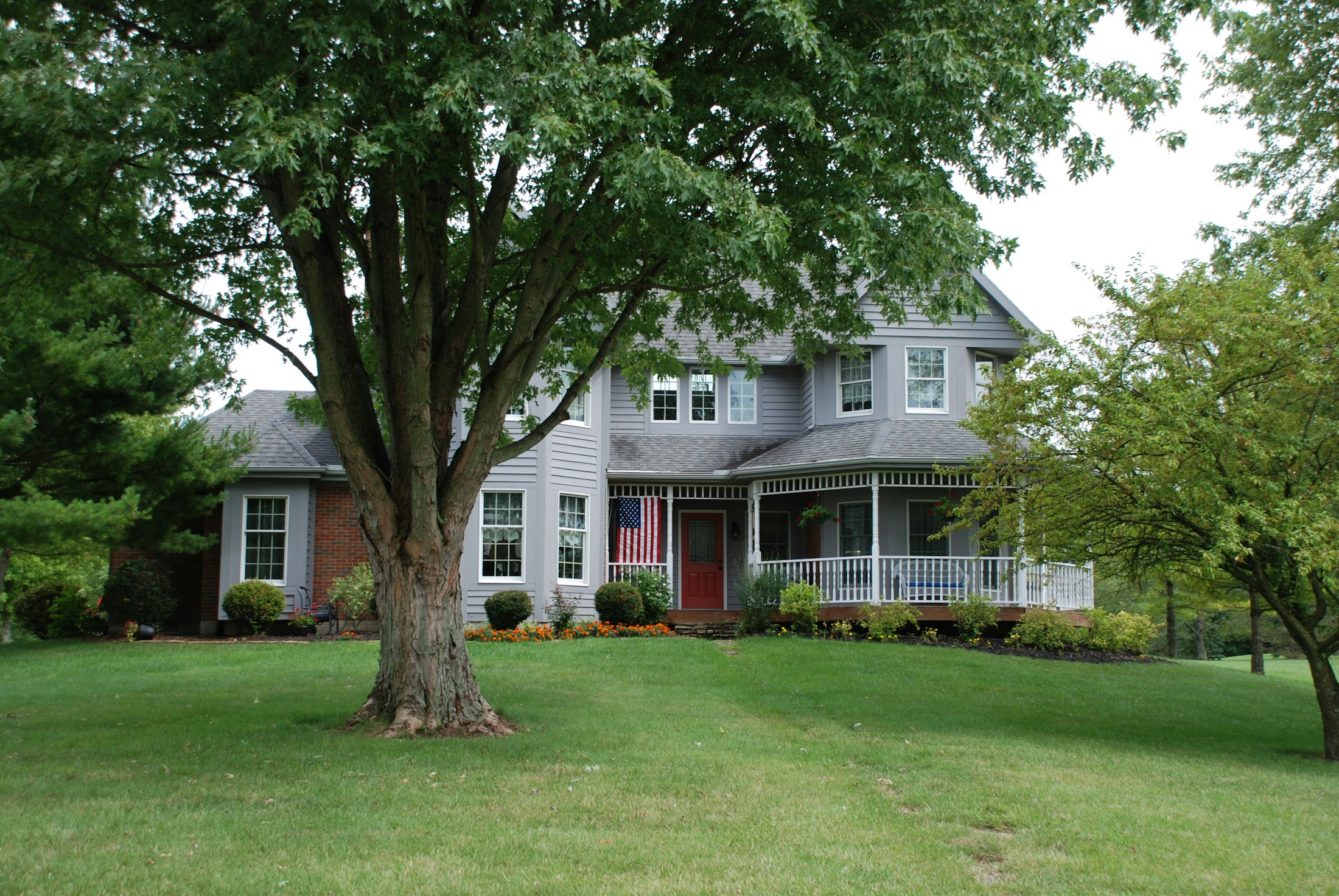 A welcoming detached home surrounded by trees and a green lawn